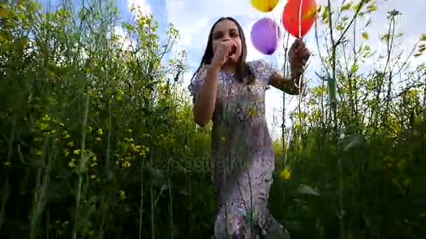 Petite fille dans une robe courant à travers le champ de blé jaune avec des ballons à la main. au ralenti — Video