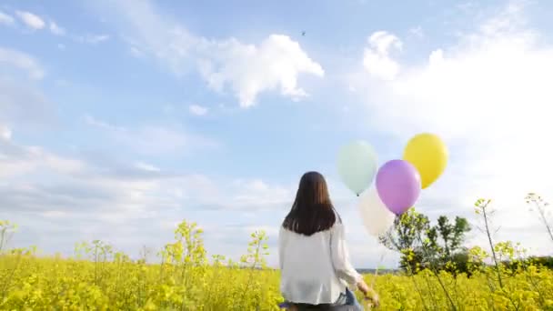 Dziewczyna z balonów na ramionach runing facet w pole rzepaku — Wideo stockowe