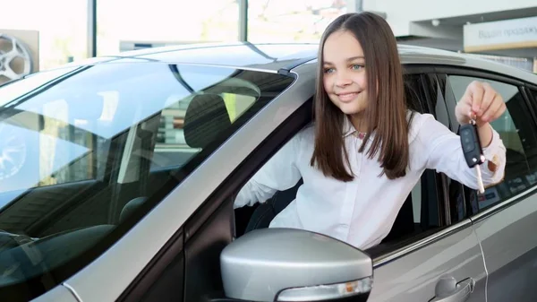 Vista lateral da linda menina olhando para longe e sorrindo enquanto sentada em um carro novo em um show de motor — Fotografia de Stock