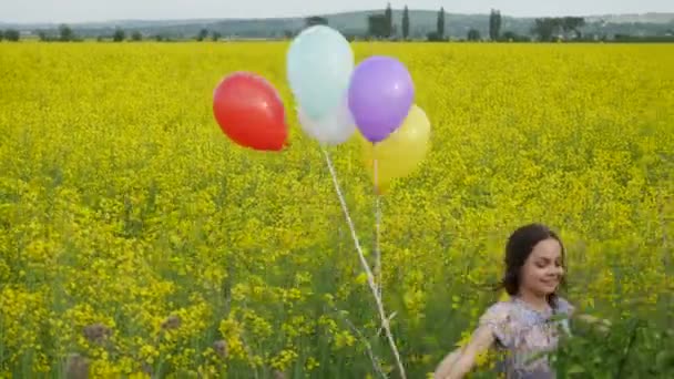 Liten flicka i en klänning som löper genom gula vetefält med ballonger i hand.slow-rörelser — Stockvideo