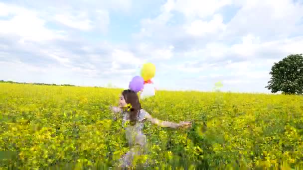 Niña en un vestido corriendo por el campo de trigo amarillo con globos en la mano — Vídeos de Stock