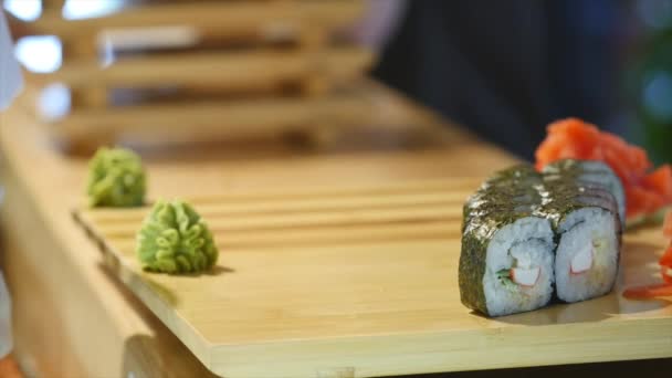 Kezében egy fából készült hajón sushi feküdt. Egy ember készül az élelmiszer az asztalra. Idő köret — Stock videók