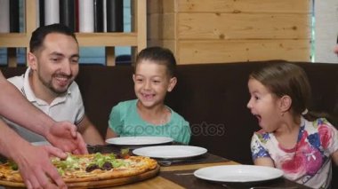 Garson kontrolden lezzetli pizza masanın üzerine koyar ve mutlu bir aile yemeye başlar. yakın çekim