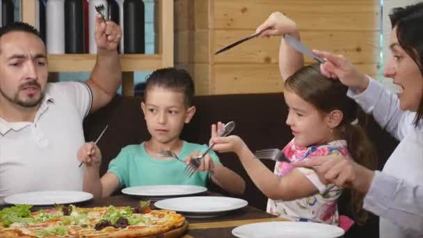 Рука официанта кладет вкусную пиццу на стол и счастливая семья начинает есть. close up — стоковое видео