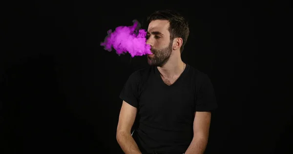 Nuori mies höyrytys elektroninen savuke ja tehdä vaaleanpunainen savu pilvet — kuvapankkivalokuva