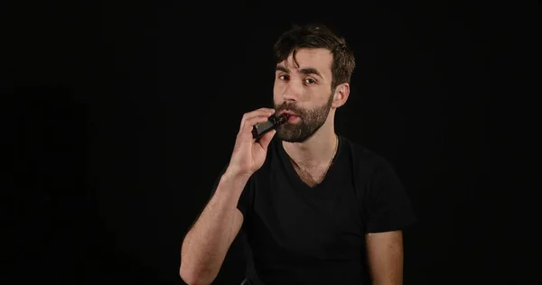 Мужчина выбирает между электронной или нормальной сигаретой на черном фоне — стоковое фото