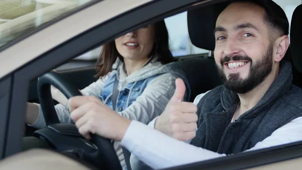 Visitando concesionario de coches. Hermosa familia está hablando y sonriendo mientras está sentado en su nuevo coche. joven muestra el dedo hacia arriba — Foto de Stock