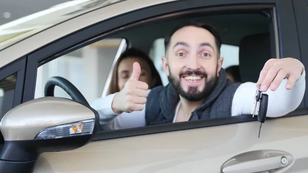 Посещение автосалона. Beautiful family is talking and smiling while sitting in their new car. молодой человек показывает пальцем вверх — стоковое фото