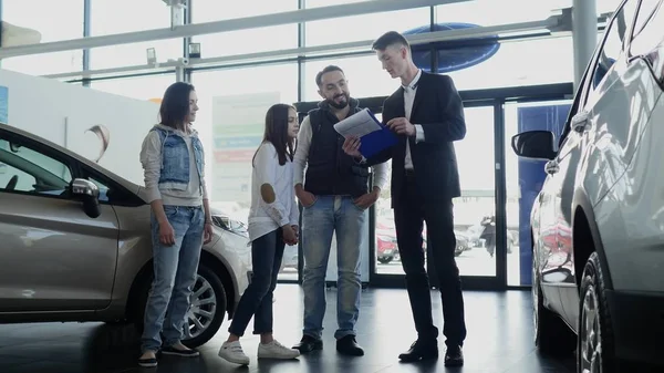 Vendedor de carros mostra uma jovem família informações sobre seu novo carro — Fotografia de Stock