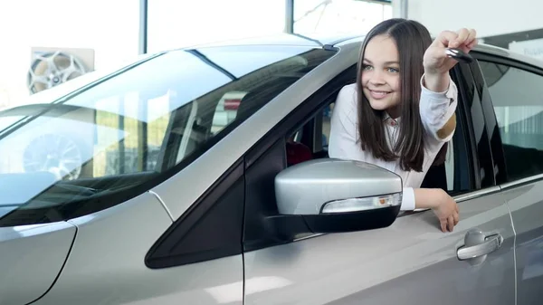 Niña feliz mostrando la llave de su auto nuevo. Auto negocio, venta de coches, la tecnología y el concepto de la gente - macho feliz con concesionario de automóviles en el salón de exposición o auto. Joven con un vendedor en un espectáculo de motor — Foto de Stock