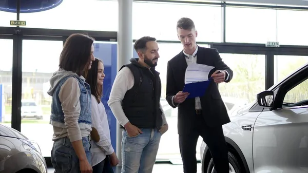 Vendedor de coches muestra a una familia joven información sobre su nuevo coche — Foto de Stock