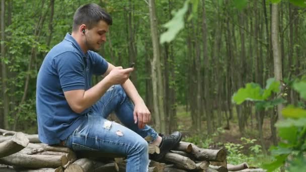 A fejhallgató a zenét hallgat egy jóképű fiatalember az erdőben — Stock videók
