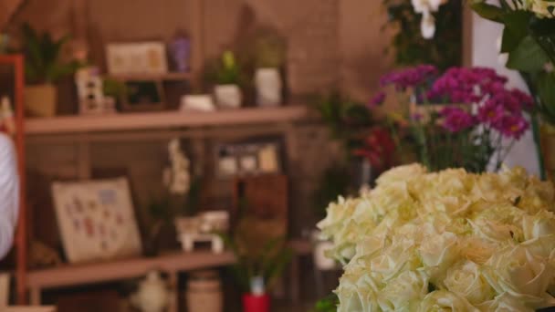 Крупный план свежих роз белого цвета с зелеными стеблями и листьями, выложенными в пучки для продажи в цветочном магазине — стоковое видео