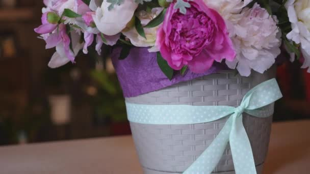 Γκρο πλαν του μπουκέτο με πολύχρωμα παιώνιες, τριαντάφυλλα και μπλε κορδέλα Λευκό τραπέζι. Σε φόντο κατάστημα λουλουδιών — Αρχείο Βίντεο