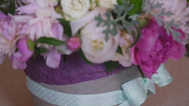 Primer plano del ramo de coloridas peonías y rosas y cinta azul en la mesa blanca. En la tienda de flores de fondo — Vídeo de stock