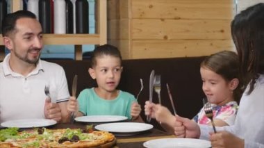 Garson kontrolden lezzetli pizza masanın üzerine koyar ve mutlu bir aile yemeye başlar. yakın çekim