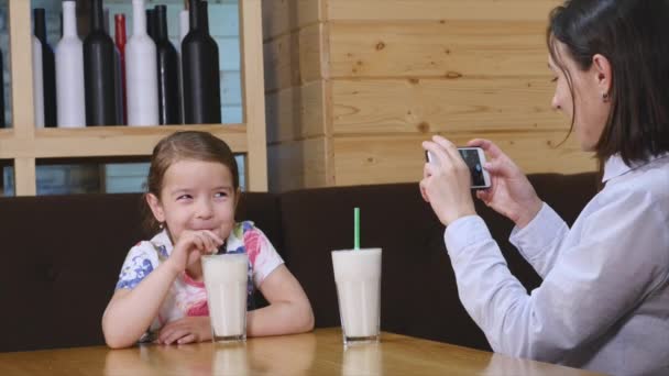 Beber cóctel infantil en el restaurante cuando la madre fotografía en el teléfono móvil — Vídeos de Stock