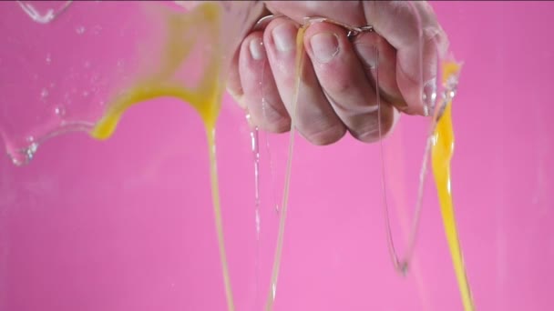 Рука, сжатая в кулаке, разрушает яйцо на розовом фоне. — стоковое видео