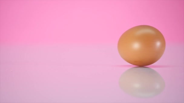 Яйцо вращается на столе на розовом фоне — стоковое видео