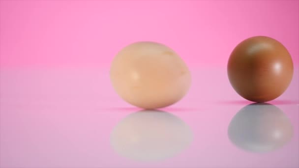 Dos huevos giran sobre una mesa sobre un fondo rosado — Vídeo de stock