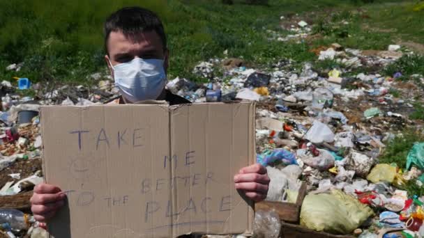 Человек в маске на мусоре держит табличку с текстом — стоковое видео