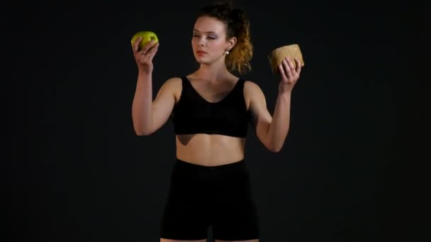 Retrato de una mujer gorda feliz eligiendo entre hamburguesa o manzana aislada sobre un fondo negro — Vídeos de Stock