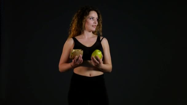 Retrato de uma mulher gorda feliz escolhendo entre hambúrguer ou maçã isolada em um fundo preto — Vídeo de Stock