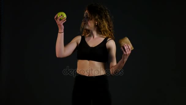 Portret van een gelukkig dikke vrouw kiezen tussen de hamburger of appel geïsoleerd op een zwarte achtergrond — Stockvideo