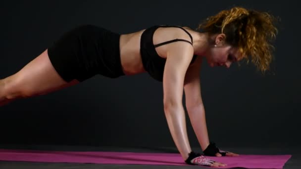 Jonge sportieve vrouw doen push-up oefening geïsoleerd op zwarte achtergrond — Stockvideo