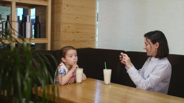 Beber cóctel infantil en el restaurante cuando la madre fotografía en el teléfono móvil — Vídeos de Stock