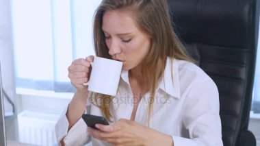 Üzerinde telefon içme kahve app ofiste gülümseyen kullanan akıllı kız. Güzel çok kültürlü genç casual kadın profesyonel üstünde hareket eden telefon