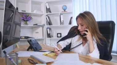 Cep telefonu üzerinde konuşurken ve Notlar not defterinde Office masada otururken yapım genç iş kadını