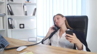 Telefonda konuşmaya ve ofiste smartphone kullanarak ve gülümseyen genç çekici iş kadını