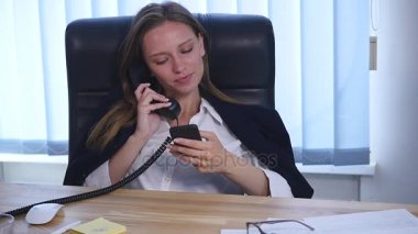 Telefonda konuşmaya ve ofiste smartphone kullanarak ve gülümseyen genç çekici iş kadını