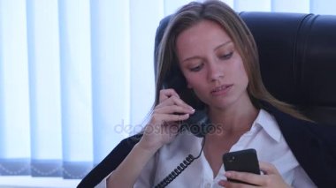 Telefonda konuşmaya ve ofiste smartphone kullanarak ve gülümseyen genç çekici iş kadını