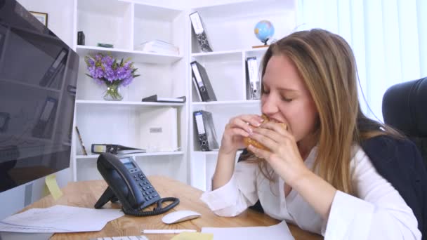 Занятая женщина за компьютером во время еды бургер — стоковое видео