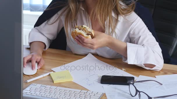 Junge Geschäftsfrau sitzt im Büro und isst einen Burger — Stockvideo