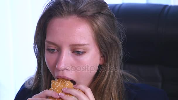 Молода бізнес-леді сидить в офісі і їсть бургер — стокове відео