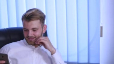 4k işadamı bir ofis koltuğu ve dokunmatik ekran smartphone üzerinde kullanır oturuyor. Erkek Beyaz gömlekli bir akıllı telefon kullanır. Teknoloji günlük yaşamda