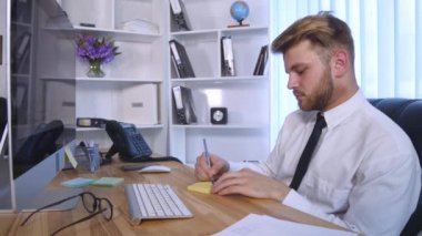 Bilgisayarda çalışarak ve Notlar not defterinde Office masada otururken yapma genç iş adamı