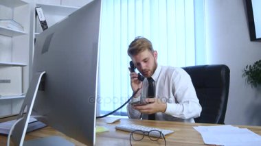 Genç iş adamı cep telefonu ve ofis telefon üzerinde konuşmak ve Notlar not defterinde Office masada otururken yapma meşgul