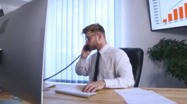 Genç iş adamı cep telefonu ve ofis telefon üzerinde konuşmak ve Notlar not defterinde Office masada otururken yapma meşgul
