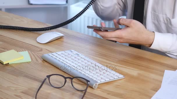 Hände eines jungen geschäftigen Geschäftsmannes, der Telefon und Bürotelefon benutzt und sich im Büro Notizen in Notizbuch macht — Stockvideo