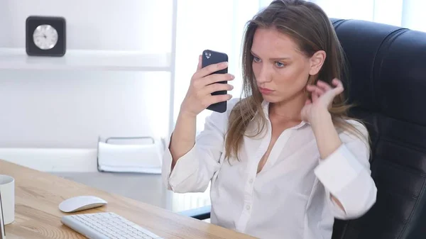 Офисная женщина чинит волосы, используя смартфон как зеркало — стоковое фото