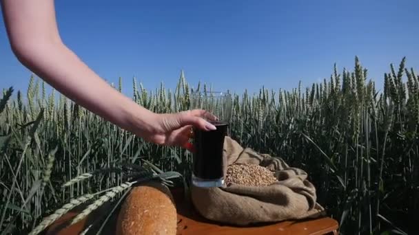 Женская рука берет стакан кваса на пшеничном фоне — стоковое видео