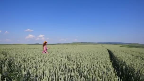 Красивая молодая женщина в шляпе, прыгающая на зеленом пшеничном поле — стоковое видео