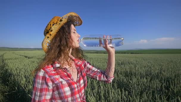 Ung kvinna dricka och svalkar sig med vatten på vetefält — Stockvideo