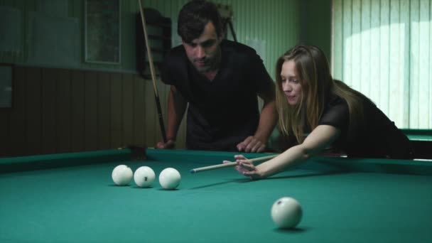 Чоловік показує свою дівчину куди вдарити м'яч - молода жінка отримує поради по стрільбі басейн м'яч під час гри в більярд — стокове відео