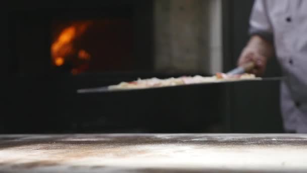 Een chef-kok zet een pizza in zijn bakstenen oven — Stockvideo