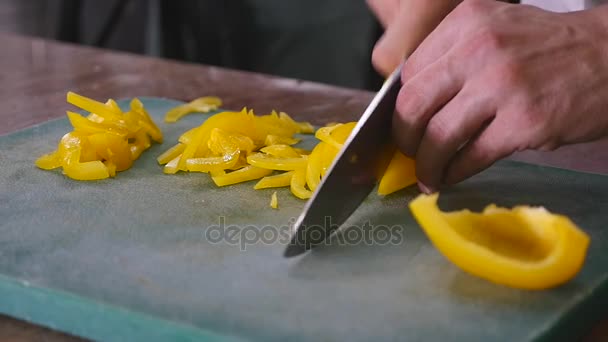 Slow motion of chef cutting yellow pepper with vegetables in the background — Stock Video